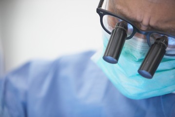 Arzt im OP-Kittel mit Mundschutz und Brille während einer OP