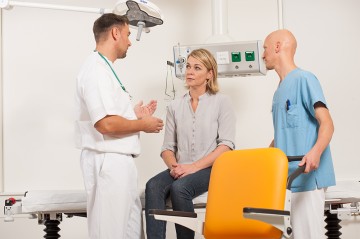 Ein Arzt und ein Pfleger sprechen mit einer Patientin, die auf einem Bett sitzt.