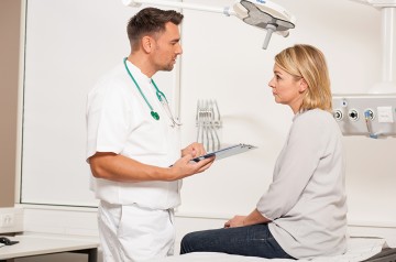 ein Arzt berät sich mit einer Patientin, die auf einer Krankenhausliege sitzt