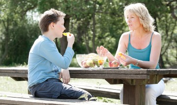 Das Bild zeigt eine erwachsene Frau und ein Kind beim Obst essen.