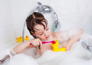 Ein Mädchen sitzt in der Badewanne und putzt mit einer Zahnbürste einer Gummiente die Zähne.