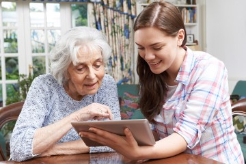 Eine junge Frau zeigt einer Seniorin die Bedienung eines Tablets