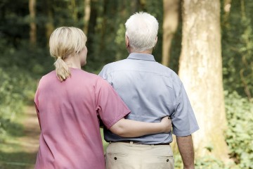 Das Bild zeigt einen Pflegebedürftigen beim Spaziergang mit einer Pflegerin.
