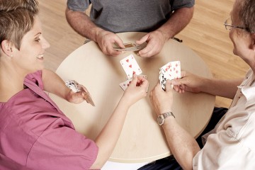 Das Bild zeigt eine Pflegerin beim Kartenspiel mit Pflegeheimbewohnern.