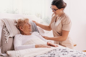 Eine junge Pflegerin am Bett, in dem eine alte Frau liegt
